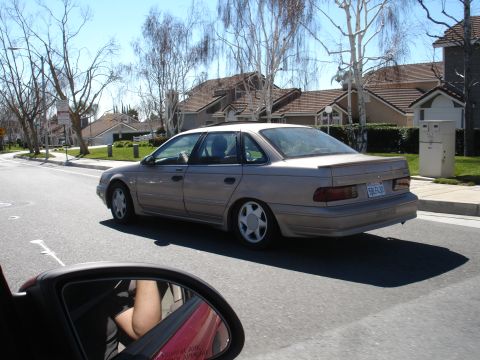 1991 Ford Taurus - The rear-side view of a tan sedan, identified as a 1992 model based on its body style.