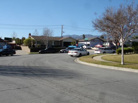 1991 Ford Taurus - Several cars are parked along a curved residential street with houses and mountains in the background.