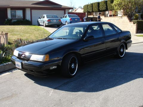 1991 Ford Taurus - Black 1991 Ford Taurus parked in front of a suburban house with two other vehicles visible.