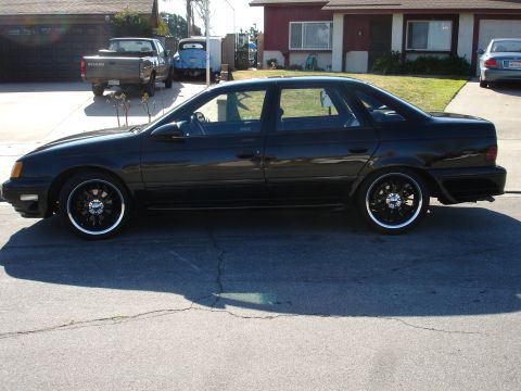 1991 Ford Taurus - A black 1991 Ford Taurus sedan is parked in front of a suburban house.