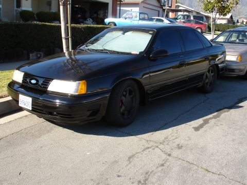 1991 Ford Taurus - This black 1991 Ford Taurus is parked on a residential street, showing its 3/4 front view with a partial view of another vehicle to its rig…
