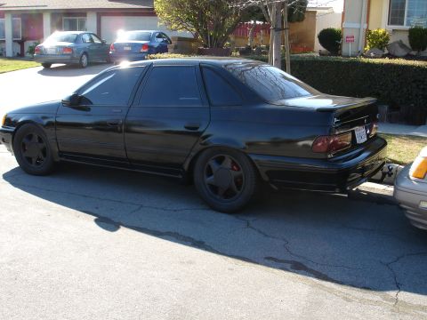 1991 Ford Taurus - This black sedan is parked on a residential street with other vehicles visible.