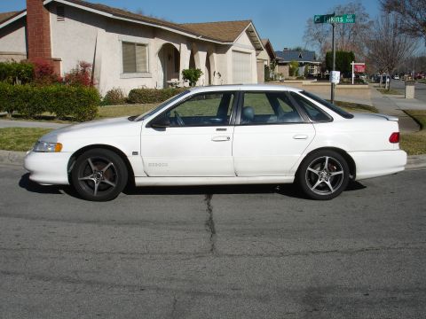 1991 Ford Taurus - A white 1991 Ford Taurus sedan is parked curbside in front of a suburban house.