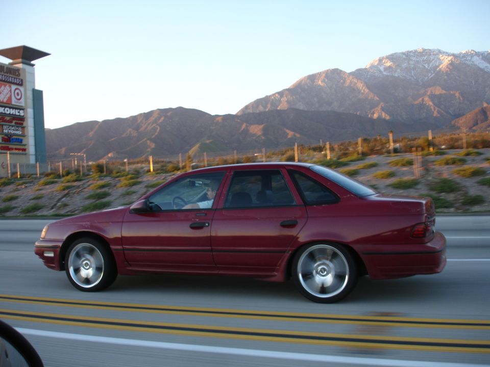 Red 1991 Ford Taurus sedan driving on highway, side view