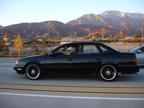 1991 Ford Taurus - Side view of a black 1991 Ford Taurus on a highway, with another car visible to the right.