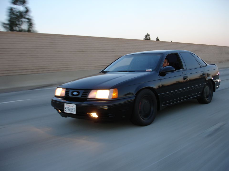 Black 1991 Ford Taurus driving on highway, front 3/4 view