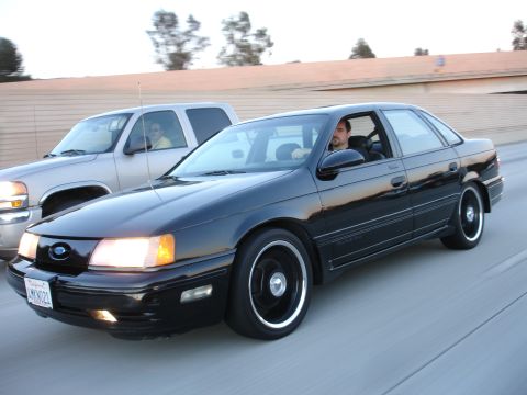 1991 Ford Taurus - Black 1991 Ford Taurus sedan in motion on a highway, with a pickup truck alongside.