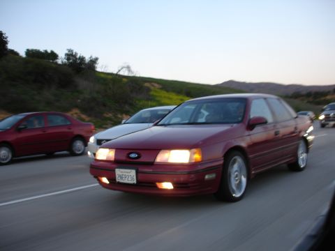 1991 Ford Taurus - A maroon 1991 Ford Taurus is seen driving on a highway with other vehicles around it.