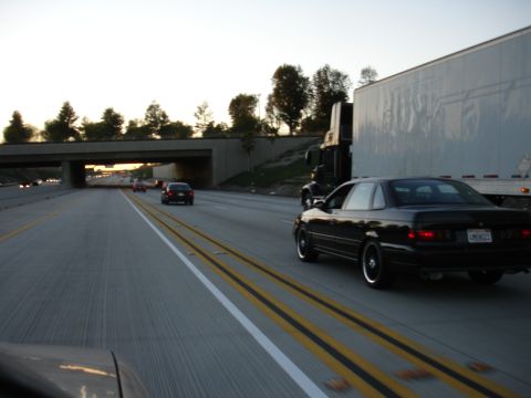 1991 Ford Taurus - A black 1991 Ford Taurus sedan is seen from behind on a highway, passing a large semi-truck.