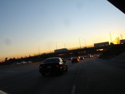 1991 Ford Taurus - A black sedan travels on a busy highway as the sun sets, casting a warm glow across the sky.