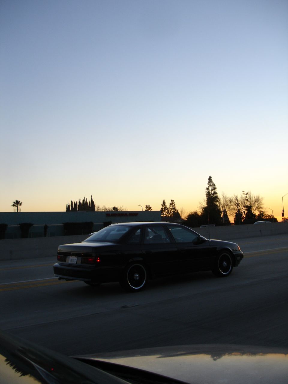 Black sedan driving on a highway at sunset, side view