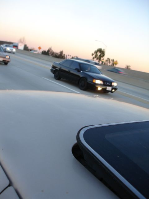 1991 Ford Taurus - A black 1991 Ford Taurus drives on the highway at dusk, with other vehicles visible.