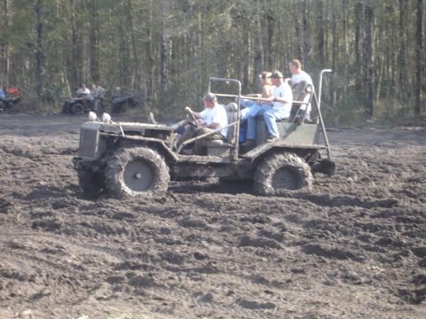1989 Ford Bronco - Several people ride in a custom off-road vehicle as it navigates a muddy terrain, with other ATVs in the distance.