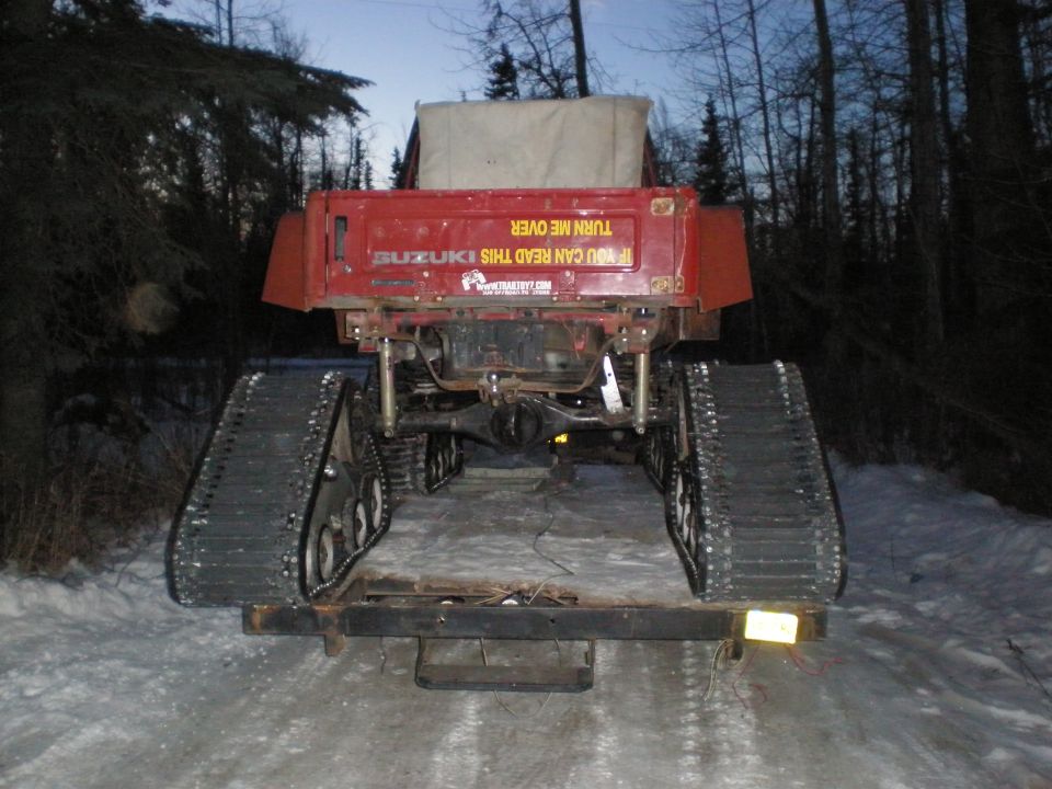 Red Suzuki Samurai on rubber tracks, rear view on snowy trail