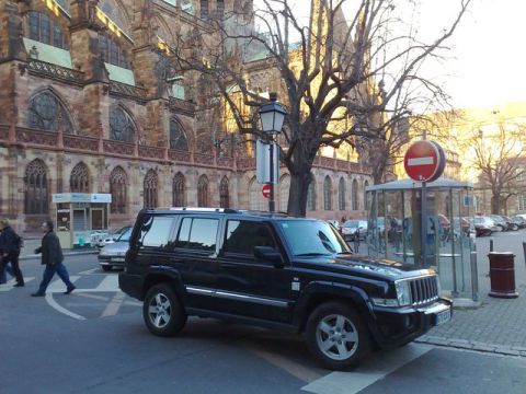 1991 Ford Crown Victoria - A black Jeep Commander is parked on a city street with a large, ornate building in the background.