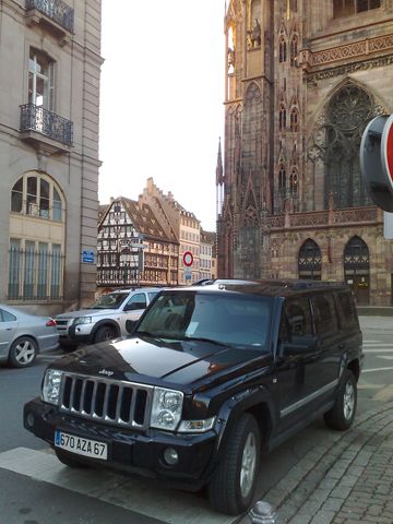 1991 Ford Crown Victoria - A black Jeep Commander is parked on a street in front of a large cathedral and historic buildings.