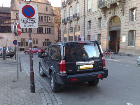 1991 Ford Crown Victoria - A black Jeep Commander is parked on a European street next to a no-parking sign.