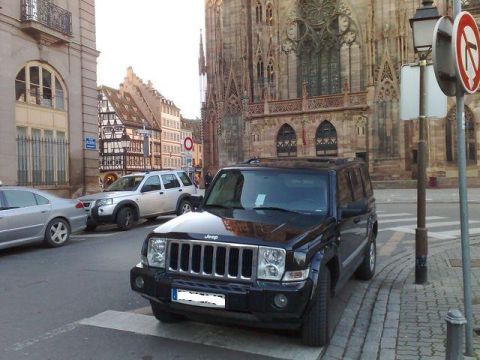 1991 Ford Crown Victoria - Jeep Commander parked on a European street with a cathedral in the background.