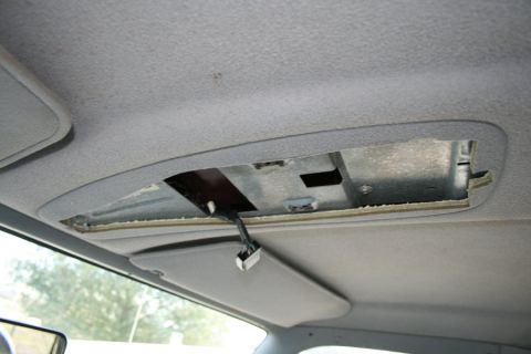 1996 Ford Bronco - The overhead console of a 1996 Ford Bronco shows an opening with exposed wiring and a partially lowered sun visor.