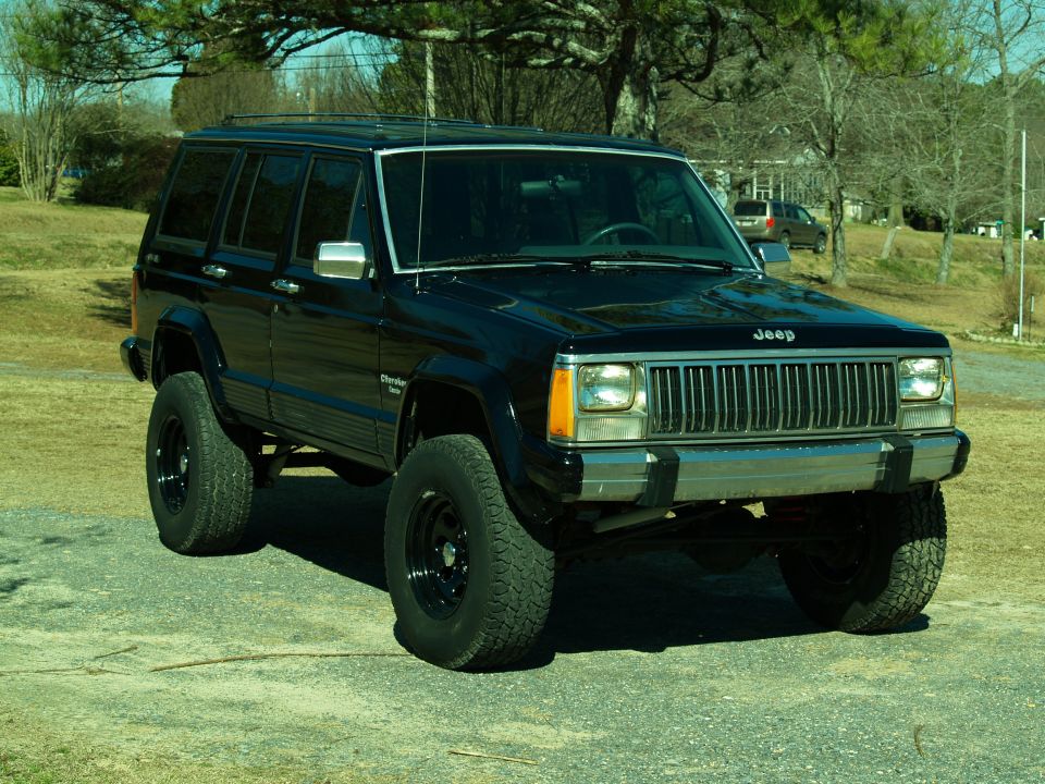 Black 1989 Jeep Cherokee with lifted suspension and off-road tires parked on gravel