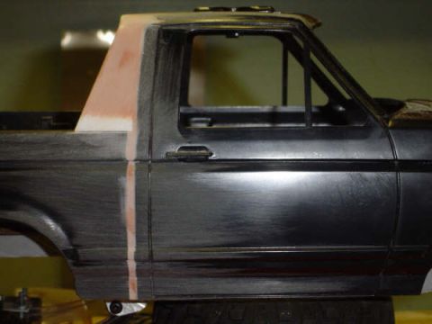 1993 Ford Bronco - Close-up of a scale model Ford Bronco body shell in bare black plastic, sanded dull with a strip of pink filler primer feathered along the…