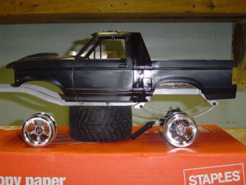 1993 Ford Bronco - Side profile of a scale model Ford truck body in glossy black plastic with the roof and rear cap removed, propped over a chassis on a Stapl…