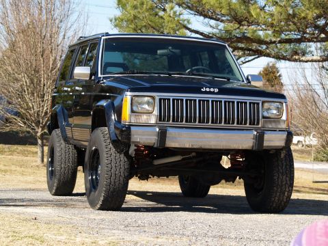 1989 Jeep Cherokee - This black 1989 Jeep Cherokee features a lifted suspension and aggressive off-road tires, presented in a front three-quarter view.