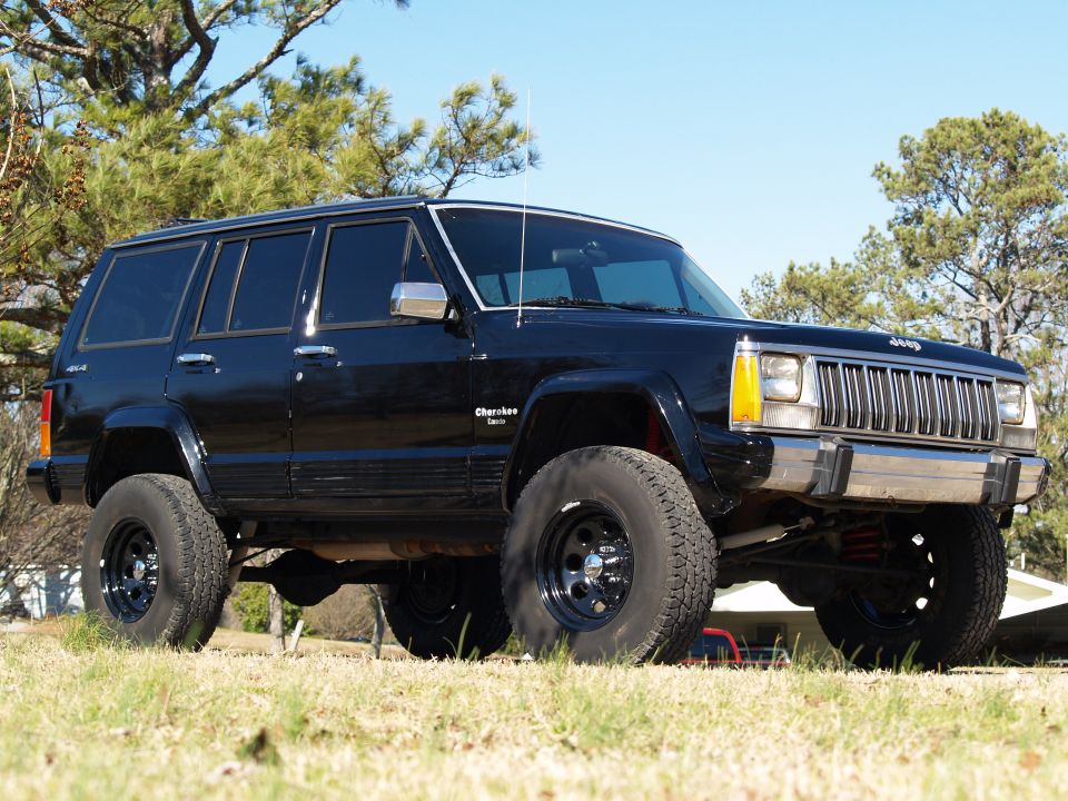 Black 1989 Jeep Cherokee with lifted suspension and aftermarket wheels parked on grass