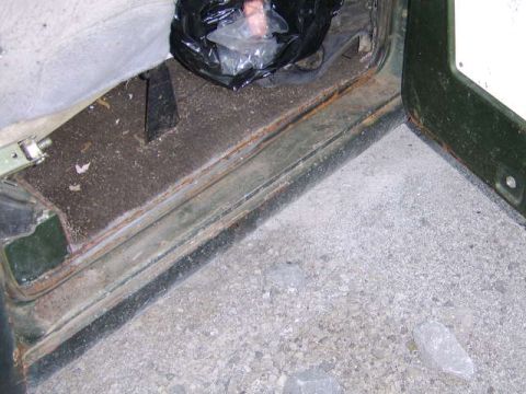 1986 Ford Ranger - The interior door sill of a vehicle shows significant rust and wear, debris, with a black plastic bag on the floor.
