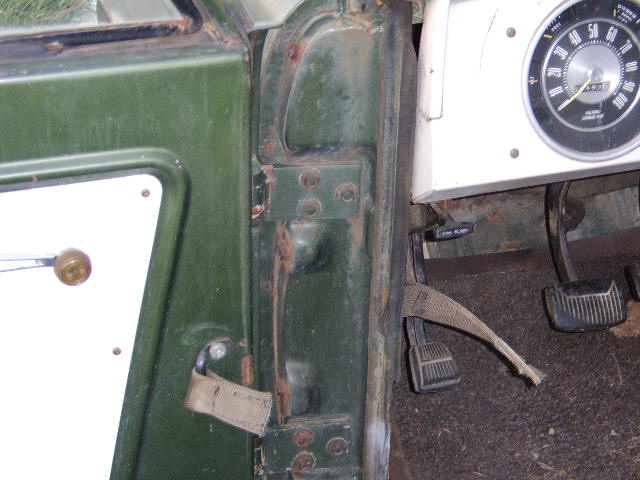 Green vehicle door interior with visible rust around hinges, and dashboard with a speedometer and pedals