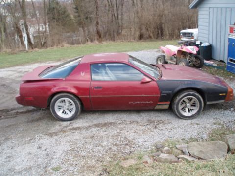 1991 Pontiac Firebird - A red and black 1991 Pontiac Firebird Formula is seen from the side, parked outdoors with a pink ATV in the background.