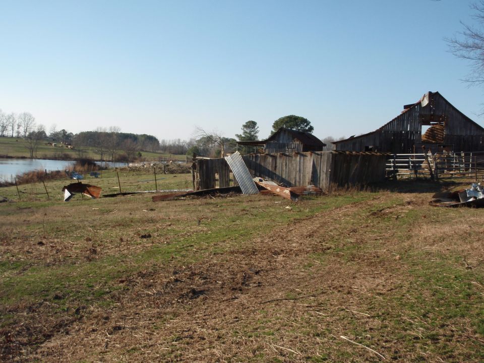 Storm-damaged weathered wooden barns with scattered metal roofing in a rural field