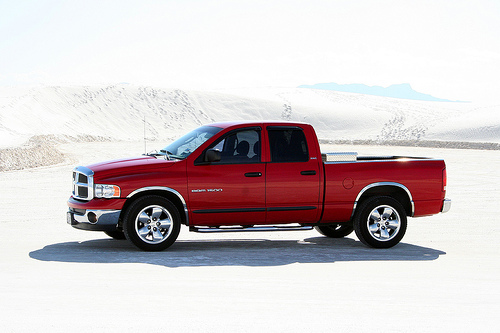 Red Dodge Ram pickup truck, side view, with chrome accents and a toolbox in the bed, parked on a sandy terrain