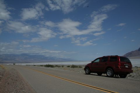 1991 Ford Crown Victoria - A red SUV is parked on the shoulder of a road in a vast, arid landscape with mountains in the distance.