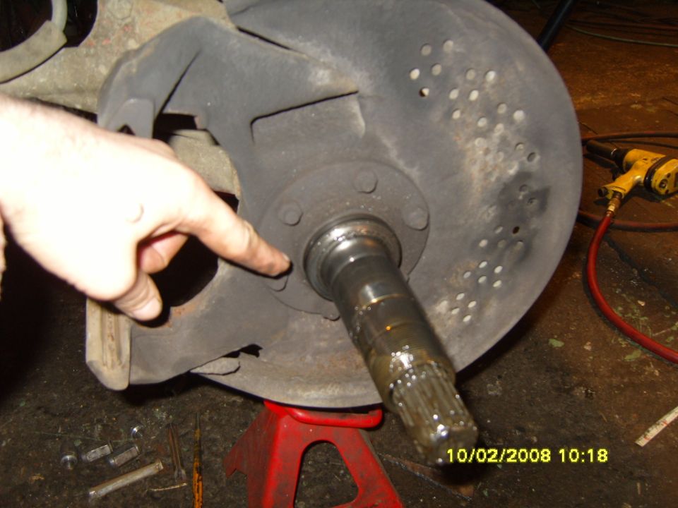 Close-up of a vehicle's spindle and brake rotor assembly, with a hand pointing to a bolt. A date stamp reads 10/02/2008