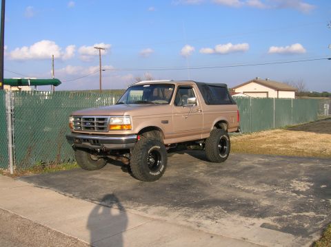 1996 Ford Bronco - This lifted 1996 Ford Bronco features a tan exterior and a black soft top, parked outdoors.