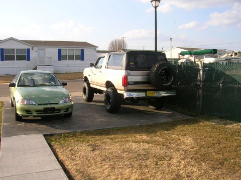 1996 Ford Bronco - A lifted Ford Bronco and a Chevrolet Cavalier are parked in a driveway next to a mobile home.