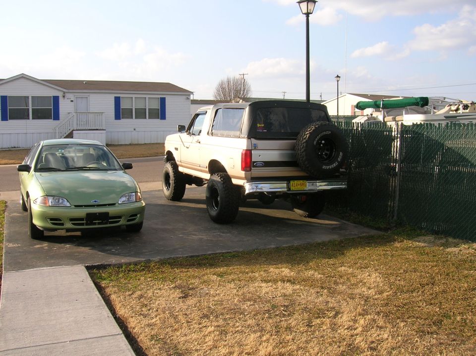 Lifted 1990s Ford Bronco parked next to a green Chevrolet Cavalier