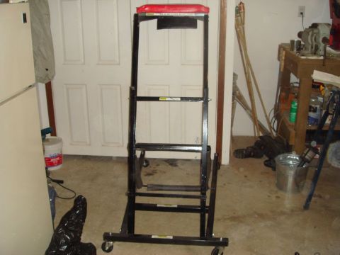 1996 Ford Bronco - A black rolling creeper seat with a red padded seat is positioned in front of a garage door.