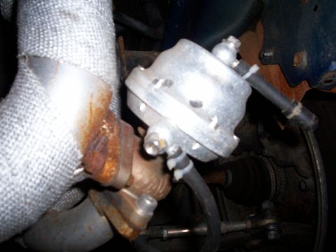 1994 Ford Probe - Close-up of a turbocharger wastegate actuator, showing rust on the exhaust manifold and heat-wrapped piping.