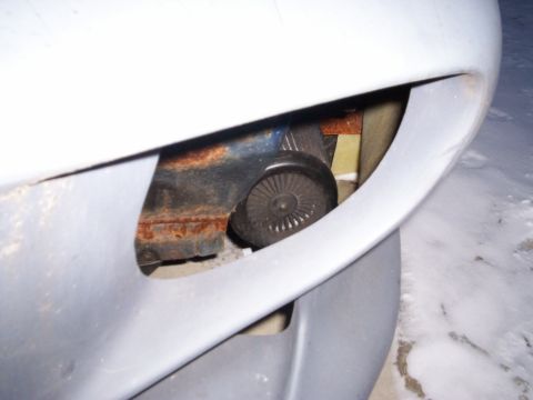 1994 Ford Probe - Visible rust on a metal bracket with a small fan-like component, seen through a car's bumper opening.