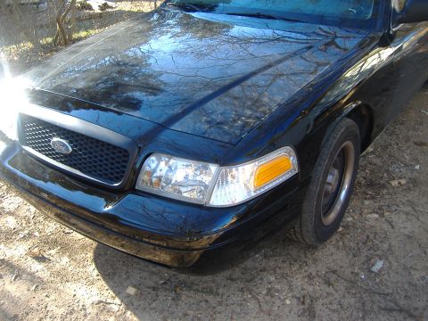 2001 Ford Crown Victoria - The front end of a black Ford Crown Victoria is shown parked outdoors on a dirt surface.