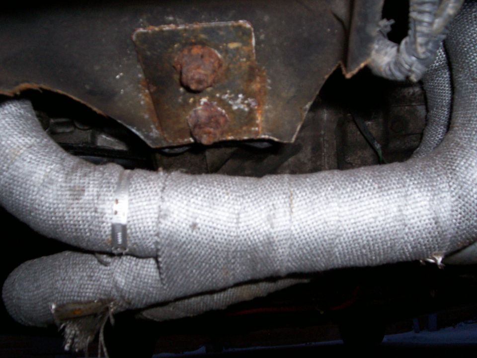 Exhaust pipes wrapped in heat-resistant material, attached to a rusty metal bracket with bolts