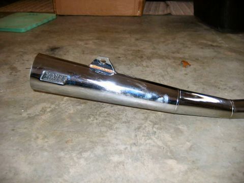 1985 Ford LTD Crown Victoria - A close-up view of a shiny chrome motorcycle exhaust pipe with a Yoshimura brand badge. It rests on a concrete floor.