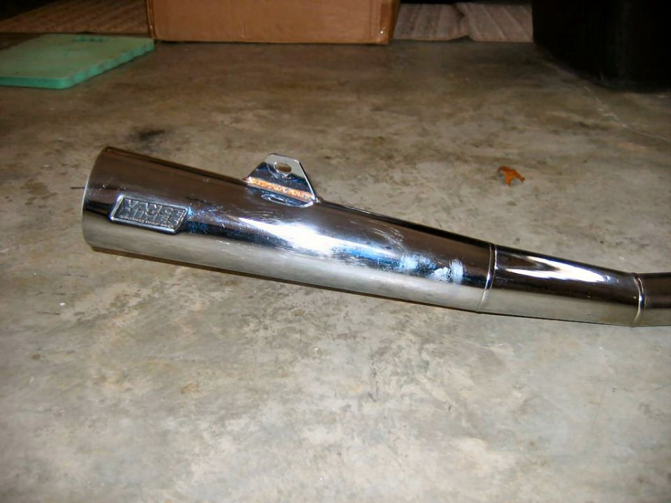 Chrome motorcycle exhaust pipe with a rectangular badge that says 'YOSHIMURA'