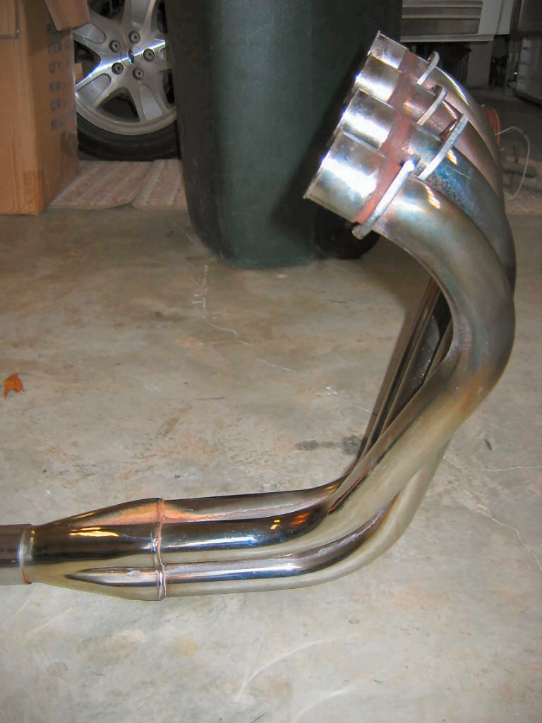 Exhaust manifold with six pipes merging into one, made of shiny metal with heat discoloration
