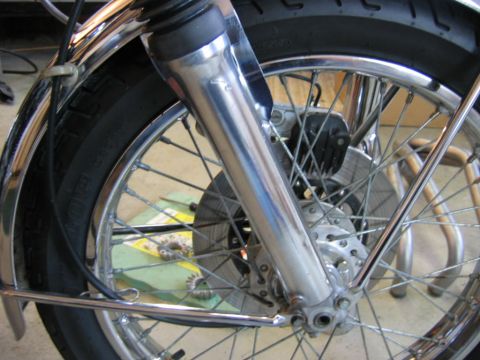 1985 Ford LTD Crown Victoria - Close-up of a motorcycle's front wheel assembly, showing the tire, spokes, and brake components.