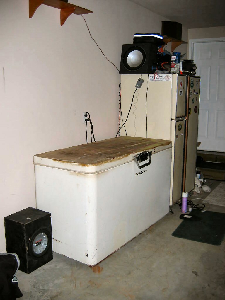Chest freezer and two refrigerators in a garage setting with speakers on top