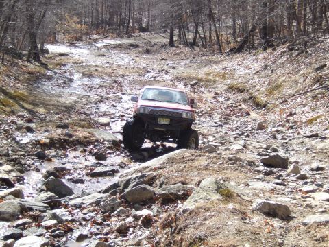 1976 Toyota Land Cruiser - Off-road vehicle tackling a challenging rocky path in a forest setting.
