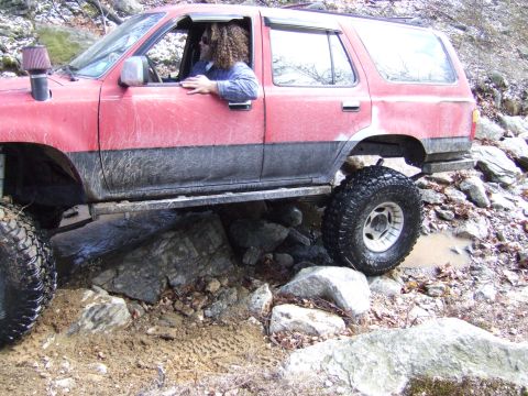 1976 Toyota Land Cruiser - This red SUV is shown from the side as it maneuvers over large rocks and mud.